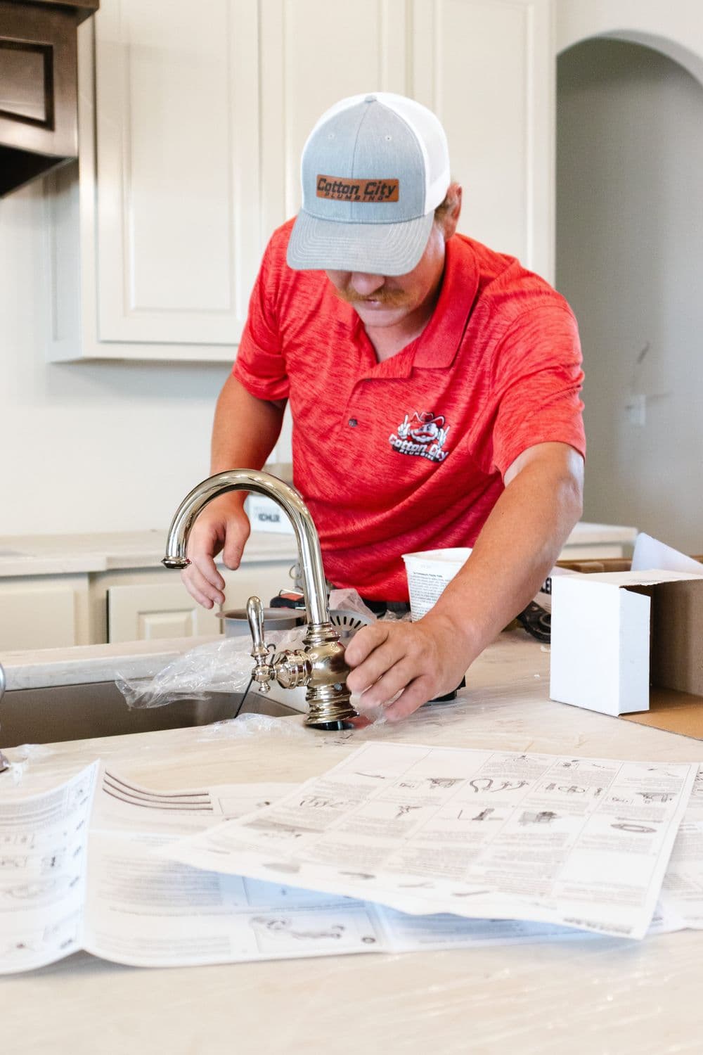 Man installing a kitchen faucet while reviewing installation instructions.
