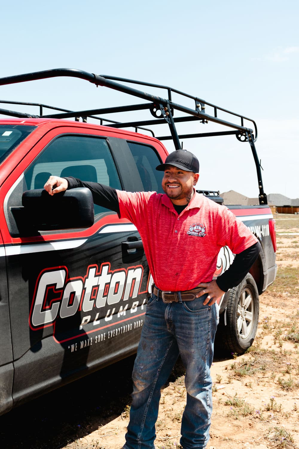 Plumber in red uniform standing by Cottonwood Plumbing truck on a sunny day.